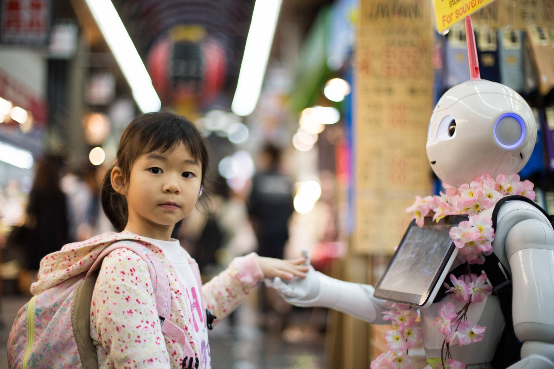 Image displaying a little girl and a robot touching hands and looking at the camera.